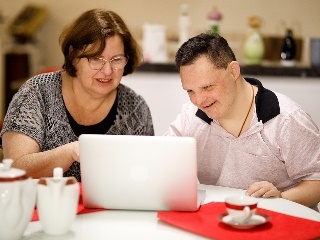 A woman helping a man look at a laptop.
