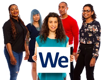 A woman standing in front of a group of people. She is holding up a sign that says 'We'.